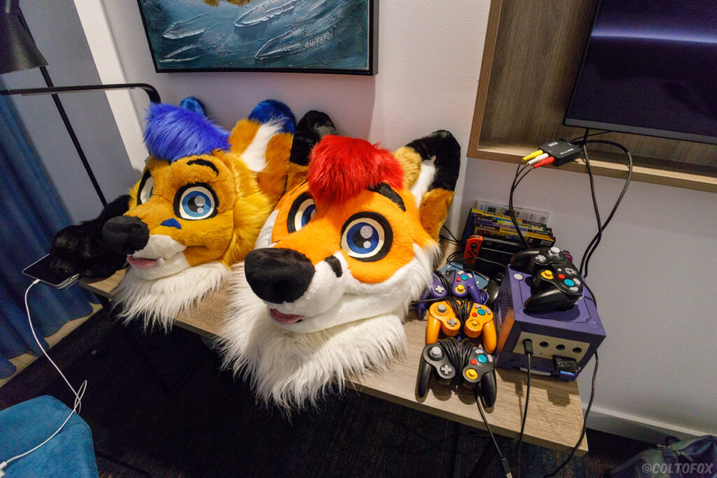 AeroFox and Colto Fox fursuit heads on a table next to a Nintendo GameCube at FurDU 2023.